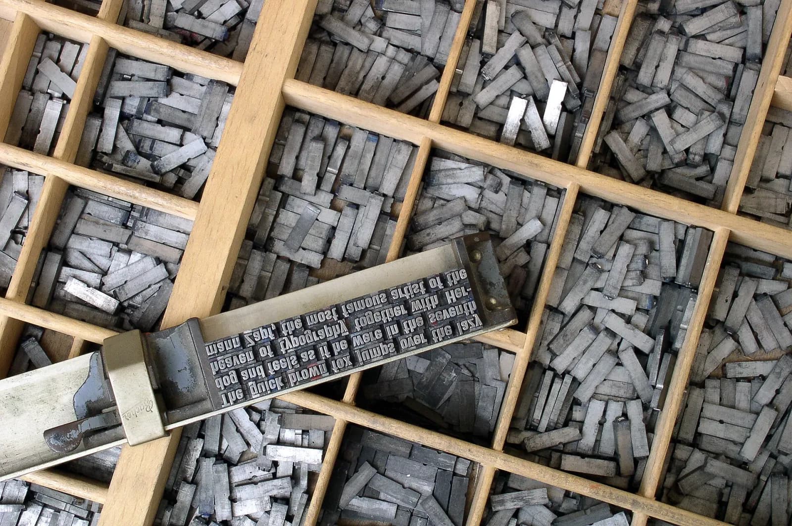 Lead type in a wooden type case, with a composing stick holding set lines on top